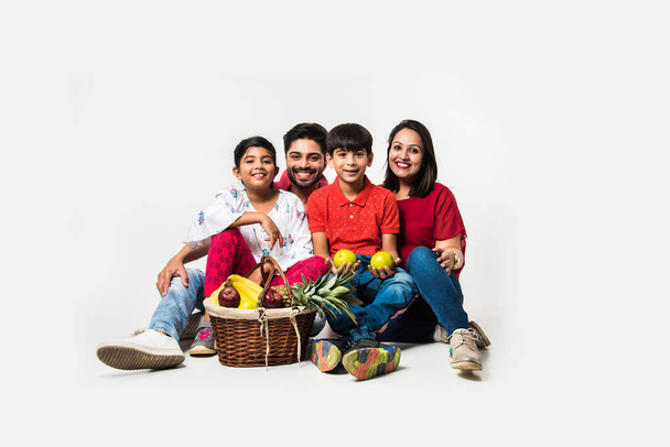 Jeune Indien Famille de quatre personnes allant pique-niquer debout sur fond blanc avec panier de fruits, tapis, football et boissons. focus sélectif
 - Photo, image