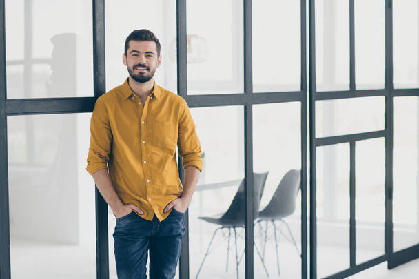 Photo of handsome guy holding hands in pockets standing in modern stylish interior apartments indoors near conference room window meeting colleagues wear casual clothes - Foto, imagen