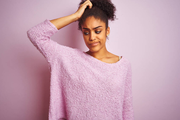 Young african american woman wearing winter sweater standing over isolated pink background confuse and wondering about question. Uncertain with doubt, thinking with hand on head. Pensive concept. - Fotó, kép