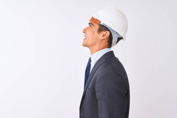 Young handsome architect man wearing suit and helmet over isolated white background looking to side, relax profile pose with natural face with confident smile. - Photo, Image