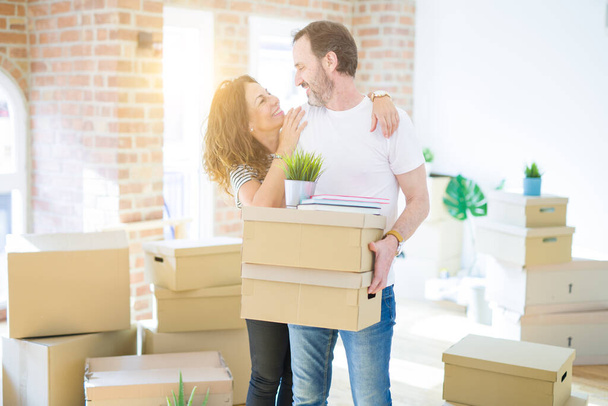 Middle age senior couple moving to a new house, holding cardboard boxing smiling happy in love with apartmant - Photo, Image