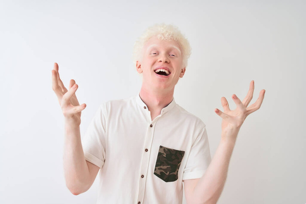 Jonge albino blonde man draagt casual shirt staan over geïsoleerde witte achtergrond vieren gek en verbaasd voor succes met armen opgeheven en open ogen schreeuwend opgewonden. Winnaars concept - Foto, afbeelding