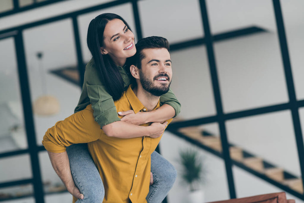 Photo of handsome husband guy and his wife lady excited to start new life in modern style interior flat indoors holding piggyback position wear casual clothes - Foto, imagen