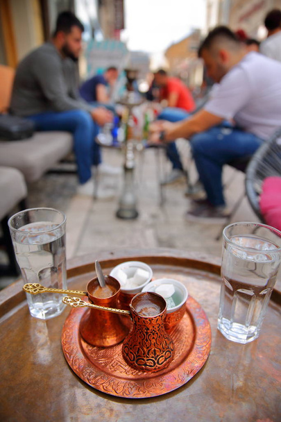 Traditional Bosnian coffee cups (with a copper tray) with young people smoking Shisha (or Hookah) in the background, Sarajevo, Bosnia and Herzegovina - Fotó, kép
