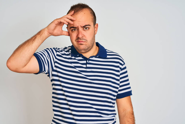 Young man wearing casual striped polo standing over isolated white background worried and stressed about a problem with hand on forehead, nervous and anxious for crisis - Photo, Image