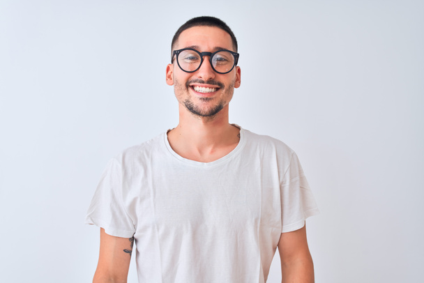 Jonge knappe man draagt een bril en staat over een geïsoleerde achtergrond met een vrolijke en koele glimlach op zijn gezicht. Geluksvogel. - Foto, afbeelding