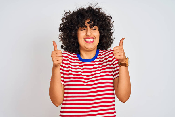 Young arab woman with curly hair wearing striped t-shirt over isolated white background excited for success with arms raised and eyes closed celebrating victory smiling. Winner concept. - Photo, Image