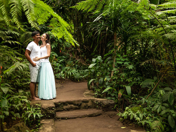 Happy smiling multiracial couple hugging and kissing on walking trail in tropical forest. Young mixed race couple on vacation in Asia. Ubud, Bali, Indonesia. - Foto, Imagen