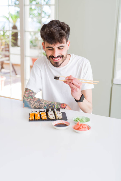 Молодий чоловік їсть суші азіатську їжу, використовуючи палички
 - Фото, зображення