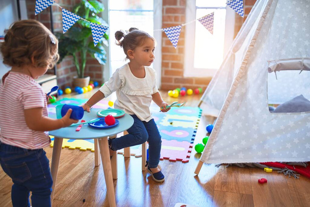 Очаровательные малыши, играющие в детские сады на пластиковой пище и столовых приборах
 - Фото, изображение