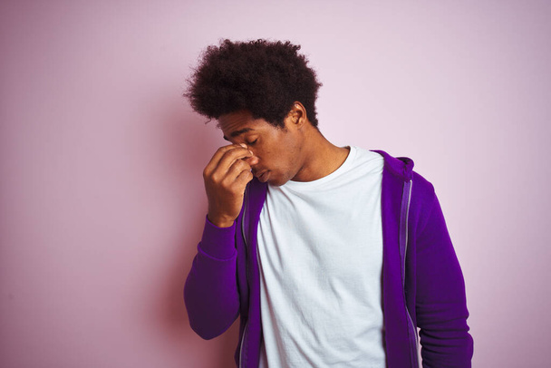 Młody Afroamerykanin w fioletowej bluzie stojący nad odizolowanym różowym tłem zmęczony pocieraniem nosa i oczu odczuwający zmęczenie i ból głowy. Koncepcja stresu i frustracji. - Zdjęcie, obraz
