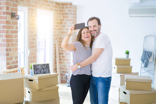 Seniorenpaar mittleren Alters zieht in ein neues Haus, hält Pappkartons und lächelt glücklich verliebt in die Wohnung - Foto, Bild