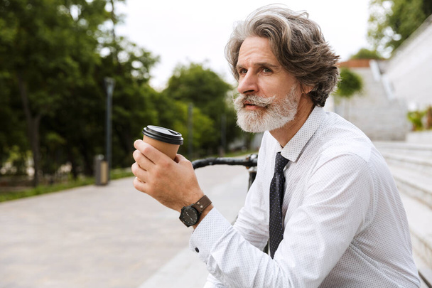 Foto van een zelfverzekerde bebaarde zakenman die koffie drinkt - Foto, afbeelding