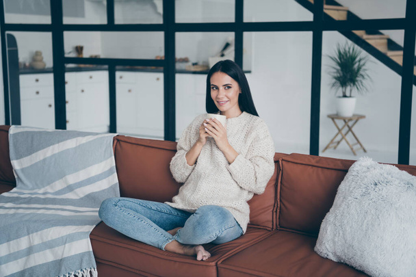 Portrait of positive girl hold cup with hot beverage enjoy winter holidays look feel content sit on brown divan in modern room - Φωτογραφία, εικόνα