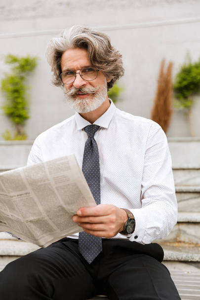 Photo of smiling elderly businessman reading newspaper - Photo, image