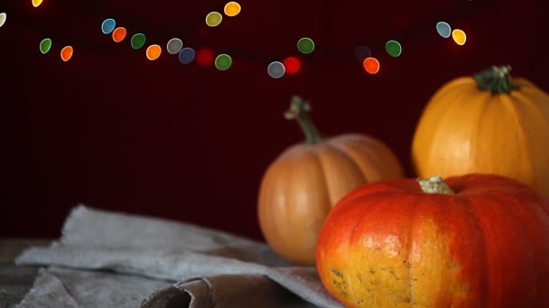 Autumn background on a dark wooden surface, three pumpkins on a background of blurry lights, selective focus - 映像、動画
