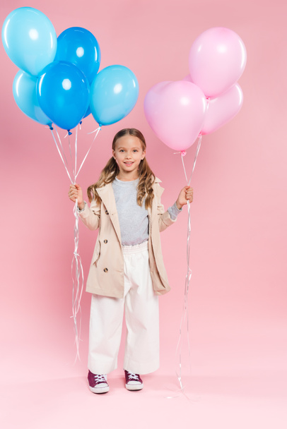 smiling kid in autumn outfit holding balloons on pink background  - Fotografie, Obrázek