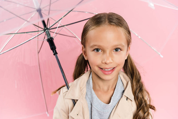 high angle view of smiling kid in autumn outfit holding umbrella isolated on pink - Photo, image