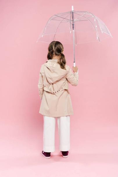 πίσω όψη του παιδιού σε φθινοπωρινή στολή κρατώντας ομπρέλα σε ροζ φόντο  - Φωτογραφία, εικόνα