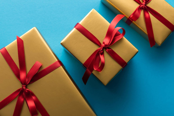 top view of golden gift boxes with red ribbons and bows on blue background - Photo, Image