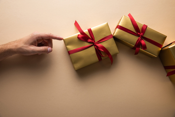 cropped view of man touching golden gift boxes with red ribbons on beige background - Foto, imagen