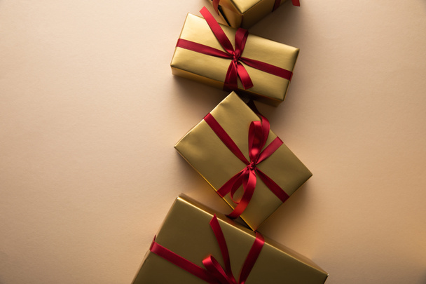 top view of golden gift boxes with red ribbons and bows on beige background - Foto, Imagem