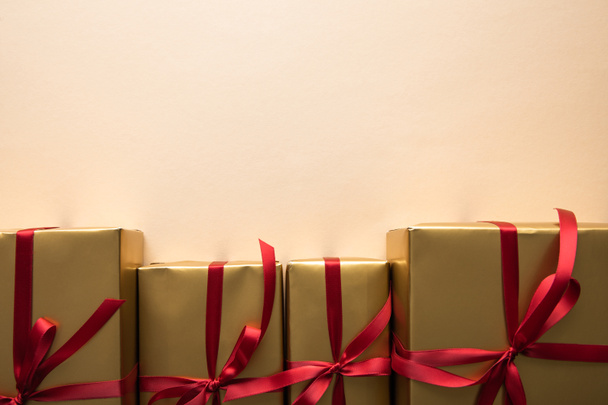 верхний вид золотых подарочных коробок с красными лентами и бантами на бежевом фоне
 - Фото, изображение