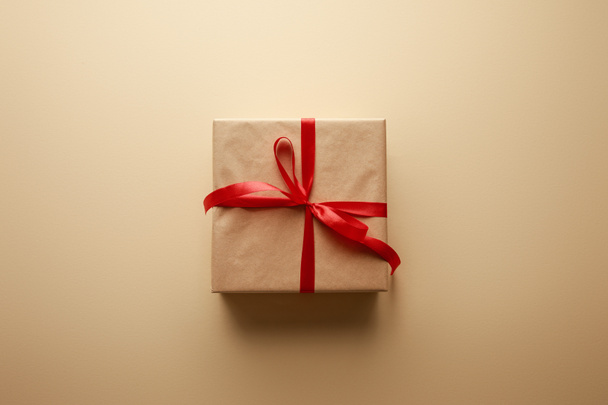 top view of gift box in craft paper with red ribbon on beige background - Fotoğraf, Görsel