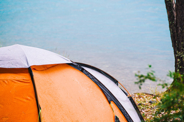 山の湖の海岸にオレンジの観光テント。森林でのハイキング、旅行のための観光機器 - 写真・画像