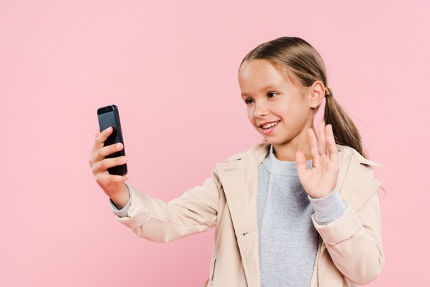 smiling and cute kid waving during video chat isolated on pink - Фото, изображение