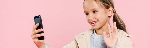 panoramic shot of smiling and cute kid waving during video chat isolated on pink - Photo, Image