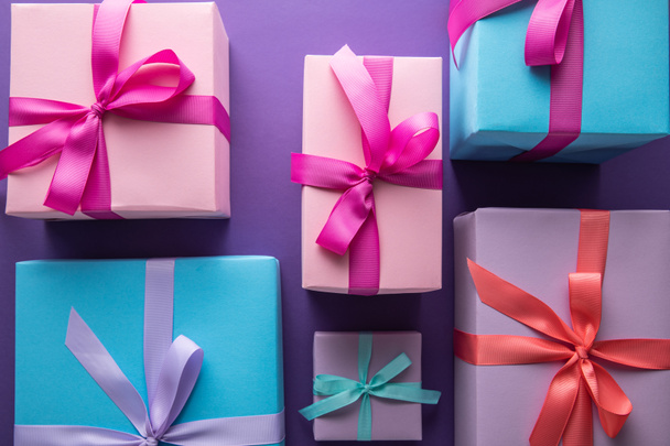 top view of colorful gift boxes with ribbons and bows on purple background - 写真・画像