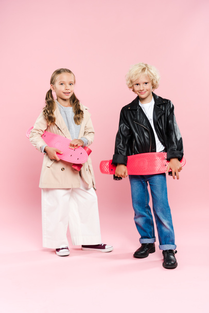 smiling and cute kids holding penny board on pink background  - 写真・画像