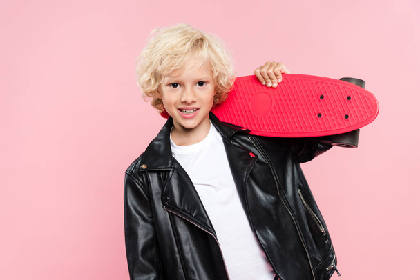 smiling and cute kid holding penny board isolated on pink - Photo, image