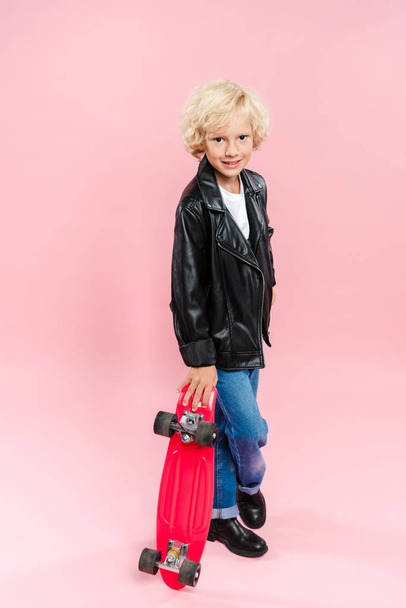 smiling and cute kid holding penny board on pink background  - Foto, immagini
