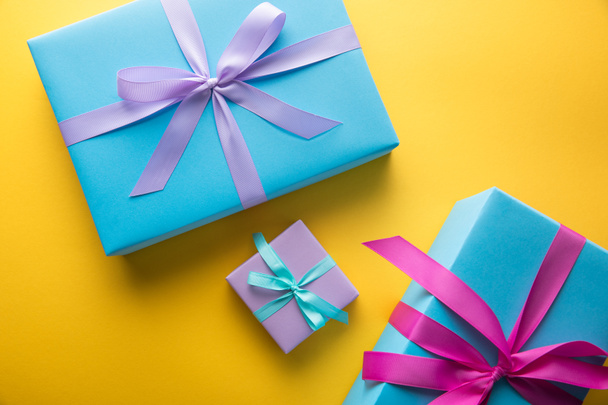 top view of multicolored gift boxes with ribbons on yellow background - Фото, зображення