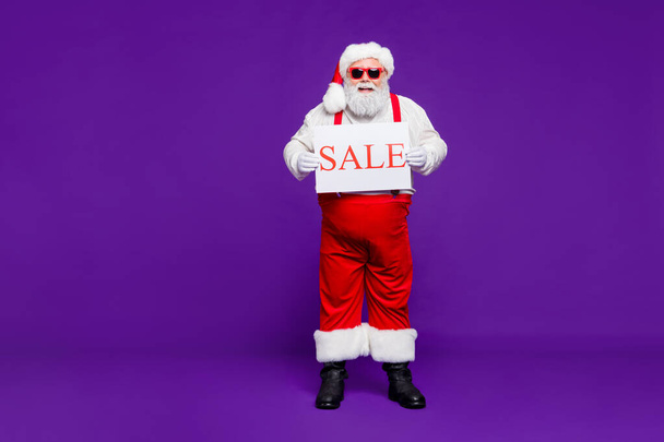 Full length body size view of his he nice confident cheerful cheery bearded thick fat Santa holding in hands demonstrating sale placard isolated on bright vivid shine vibrant violet lilac background - Фото, зображення