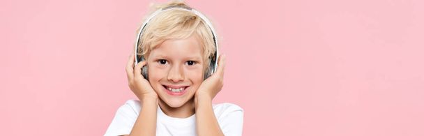 panoramic shot of smiling kid with headphones listening music isolated on pink - Фото, изображение