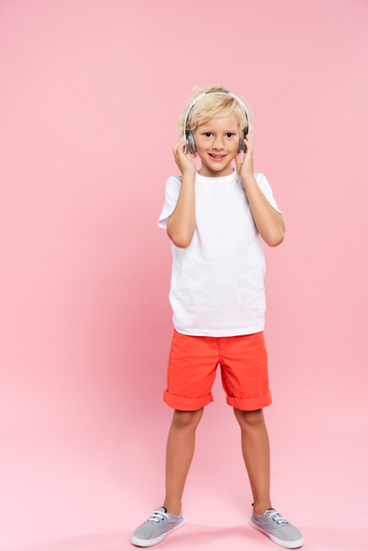 smiling kid with headphones listening music on pink background  - Valokuva, kuva
