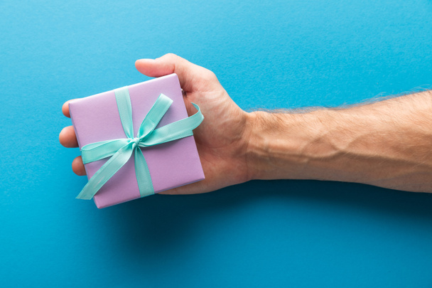 cropped view of man holding violet gift box on blue background - Фото, зображення