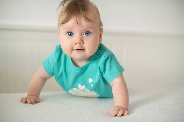 Adorable petite fille caucasienne aux yeux bleus essayant de se lever et de marcher, regardant la caméra calmement avec un sourire ; expressions faciales de bébé mignon et étapes d'apprentissage ou concepts de maternité et de famille
 - Photo, image