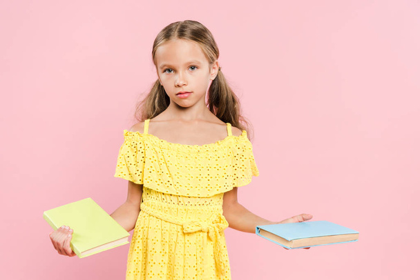 kid holding books and looking at camera isolated on pink - Photo, Image
