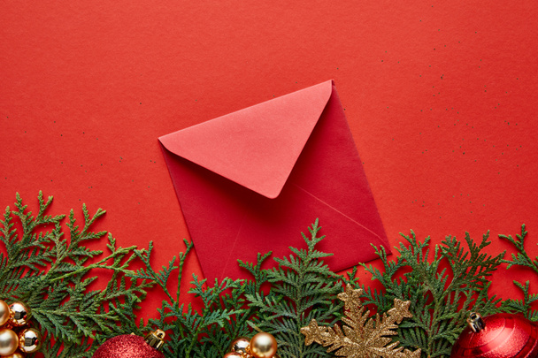 コピースペースと赤い背景に光沢のあるクリスマスの装飾、封筒とthujaのトップビュー - 写真・画像