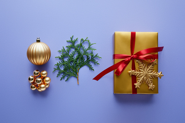 top view of shiny golden Christmas decoration, green thuja branches and gift box on blue background - 写真・画像