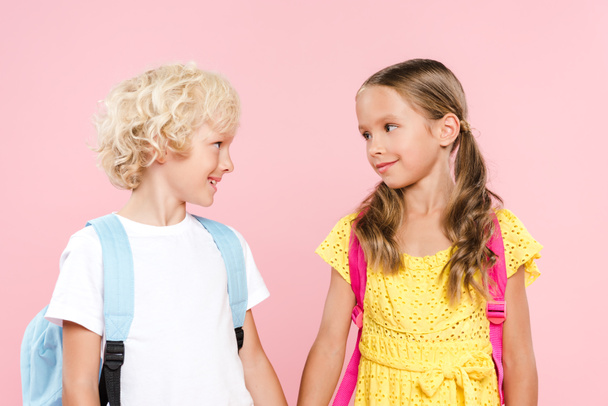 smiling schoolchildren with backpacks looking at each other isolated on pink - Photo, Image