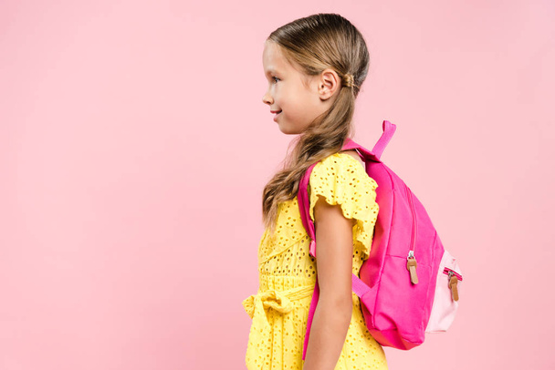 side view of smiling schoolgirl with backpack isolated on pink - Foto, Imagem