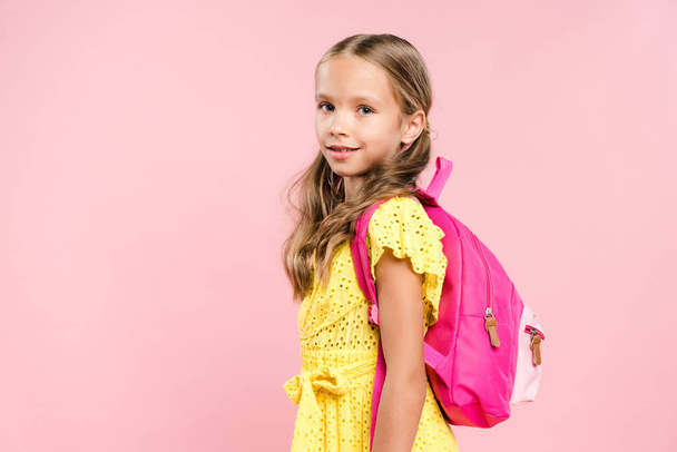 smiling schoolgirl with backpack looking at camera isolated on pink - 写真・画像
