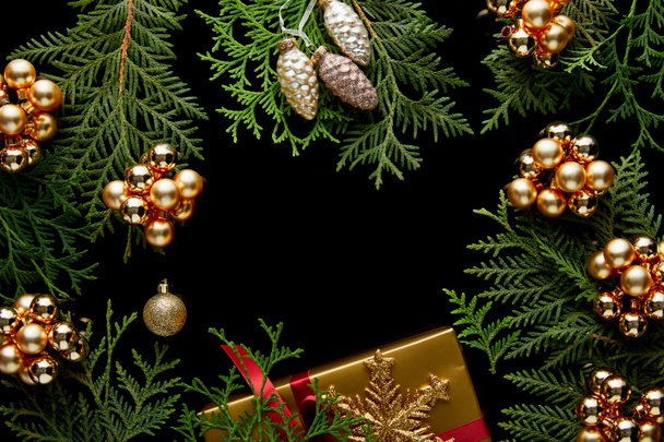 top view of shiny golden Christmas decoration, green thuja branches and gift box isolated on black with copy space - Photo, Image