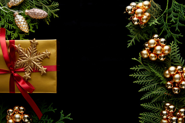felső nézet fényes arany karácsonyi dekoráció, zöld thuja ágak és ajándék elszigetelt fekete másolási hely - Fotó, kép