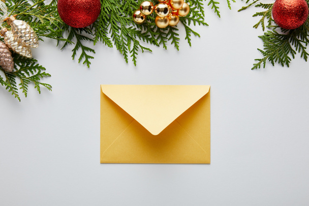 верхний вид блестящего золотистого рождественского украшения и конверта рядом с зелеными ветвями туи изолированы на белом
 - Фото, изображение